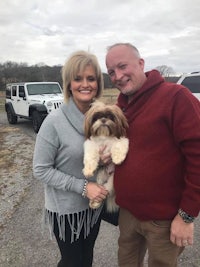 a man and woman posing with a dog in front of a jeep