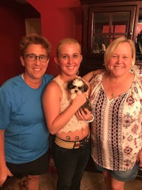 three women posing with a dog in a living room