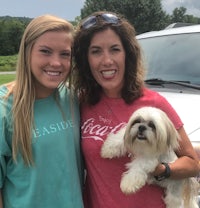 two women standing next to a white dog in front of a car