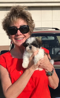 a woman in sunglasses holding a small dog in front of a car