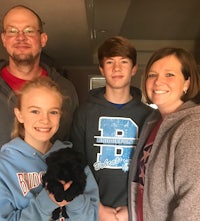 a family is posing for a picture with a black puppy