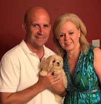 a man and woman posing with a small puppy