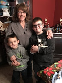 a woman holding a boy and a dog in a living room