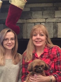 two women standing in front of a fireplace with a dog