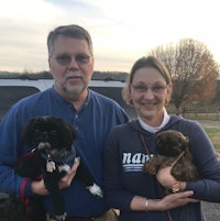 a man and woman standing in front of a truck with two small dogs