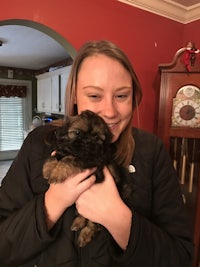 a woman holding a small puppy in a kitchen