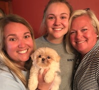 three women are smiling while holding a small dog